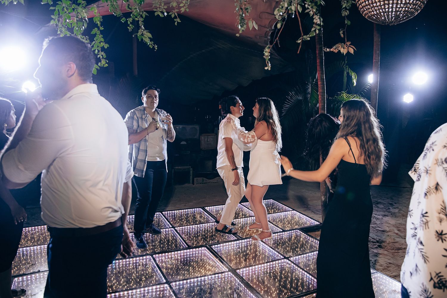 Guests dancing and celebrating on an LED-lit dance floor under disco balls and ambient lighting.
