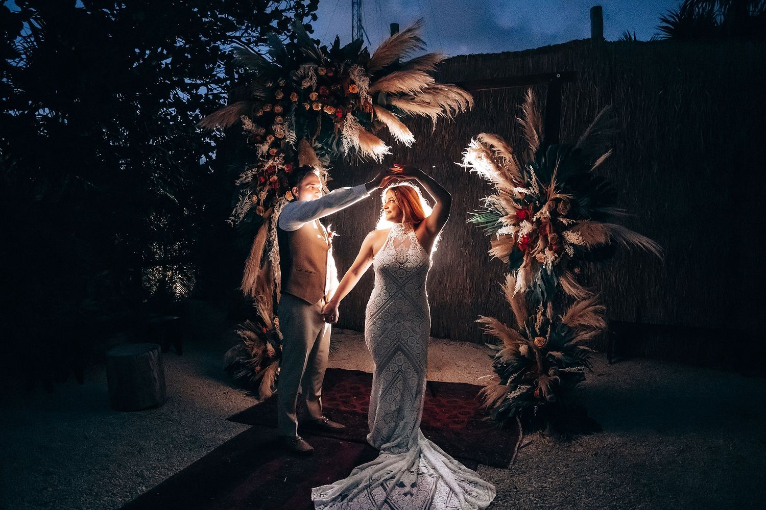 Tropical beach wedding setting at dusk with palm trees and ambient lighting.