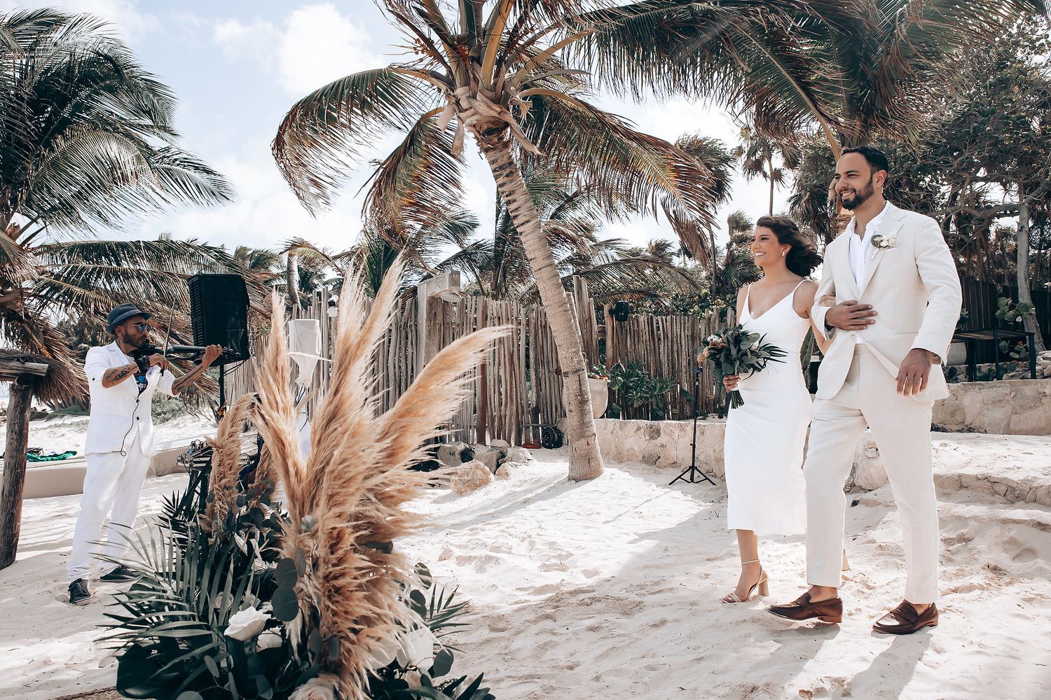 Elegant beach ceremony with boho-style decor featuring pampas grass and palm trees.