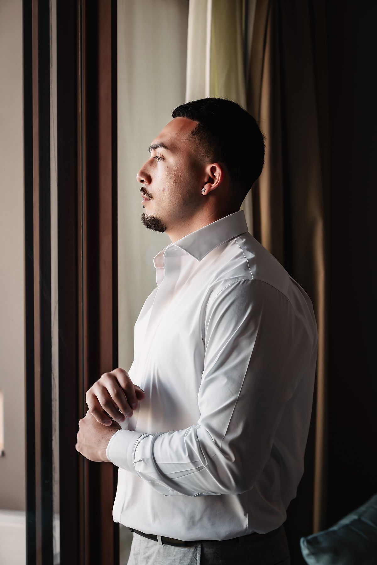Person in white dress shirt adjusting collar near window.