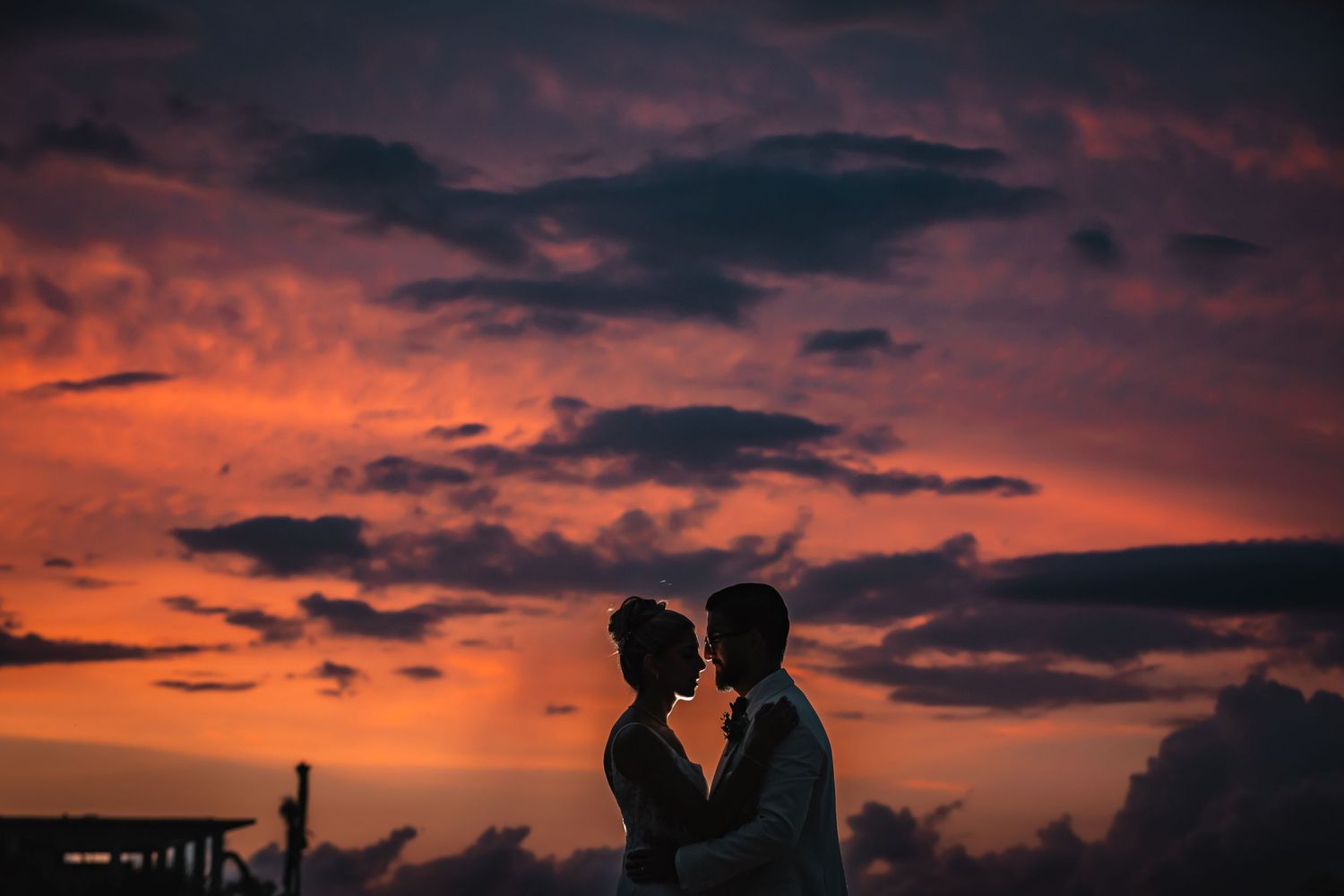 Dramatic sunset sky with vibrant orange clouds and silhouetted palm trees against a dark horizon.