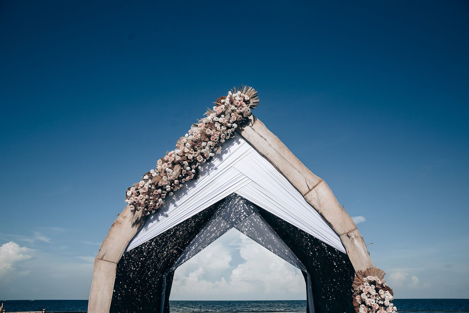 Wedding arch decorated with white flowers against vibrant blue sky at outdoor ceremony.