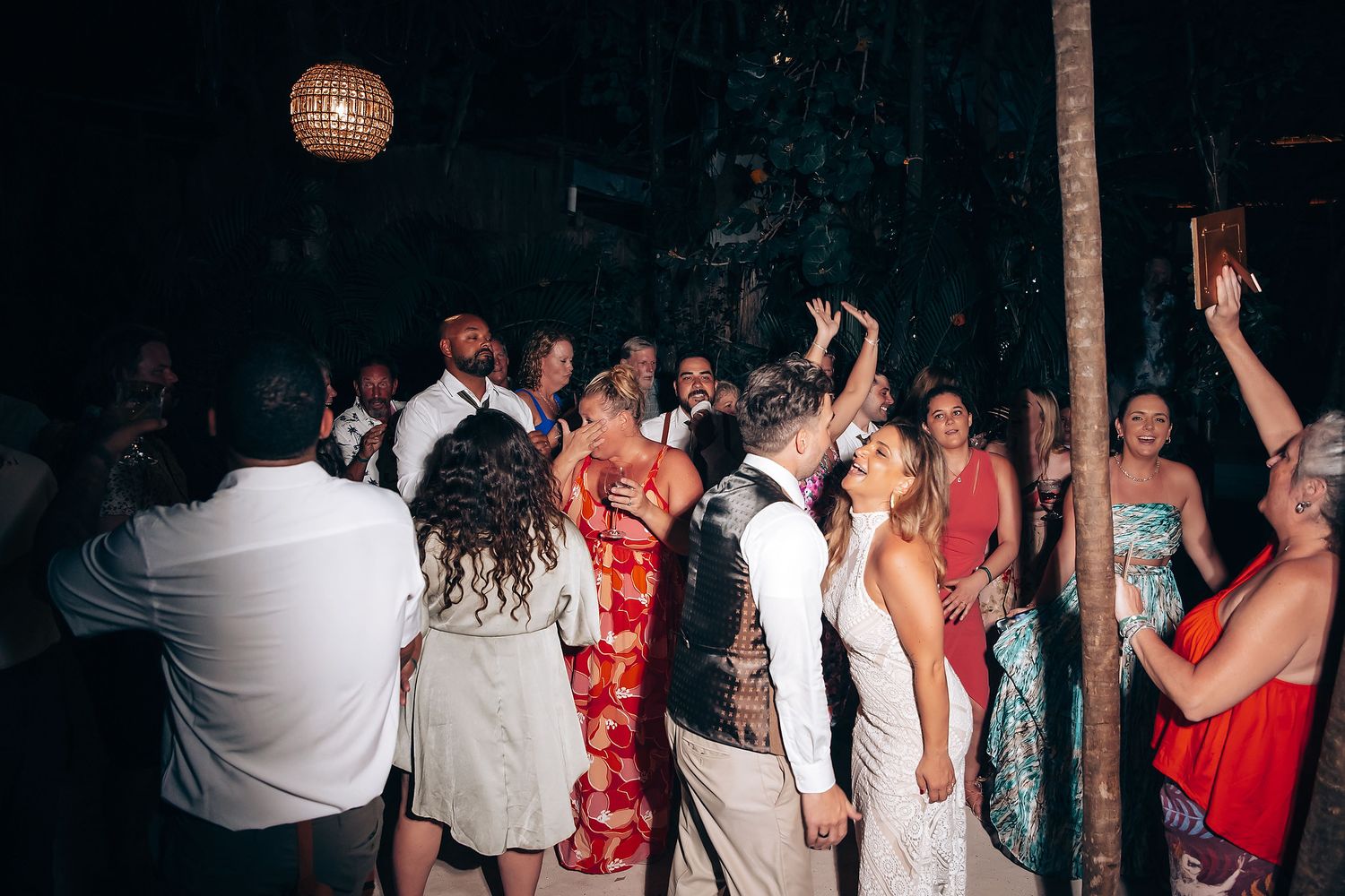 A group of people dancing and celebrating at a dimly lit party venue with red lighting effects.