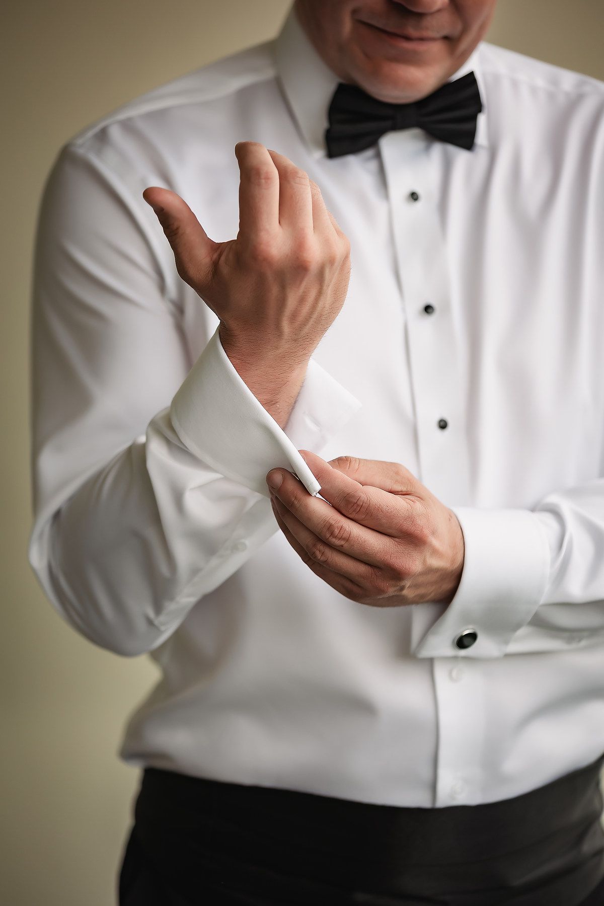 Close-up shots of someone adjusting cufflinks and bow tie while wearing a formal white tuxedo shirt.