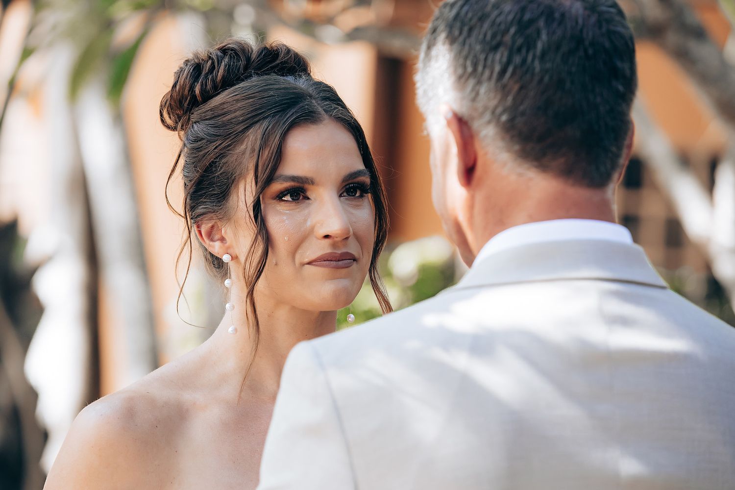 A bride and groom share a tender moment during their outdoor wedding ceremony with guests looking on.