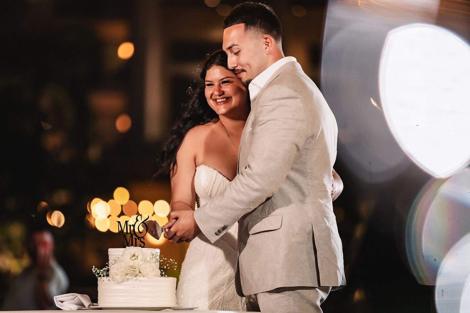 Bride and groom cutting white wedding cake together at romantic evening reception.