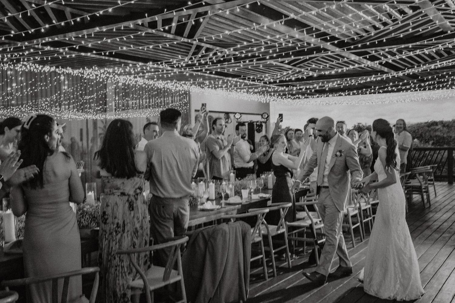 Black and white photo of bride and groom dancing at outdoor wedding reception with string lights overhead.
