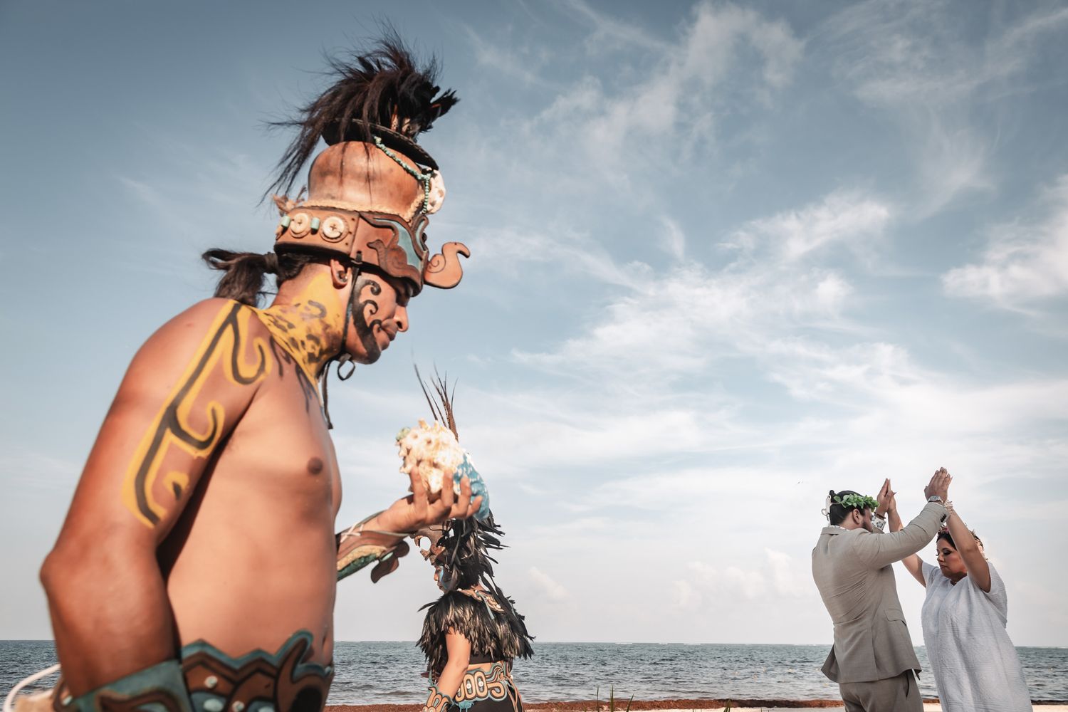 Indigenous Mayan dancers in traditional costumes perform a ceremony by the ocean at a beach wedding.