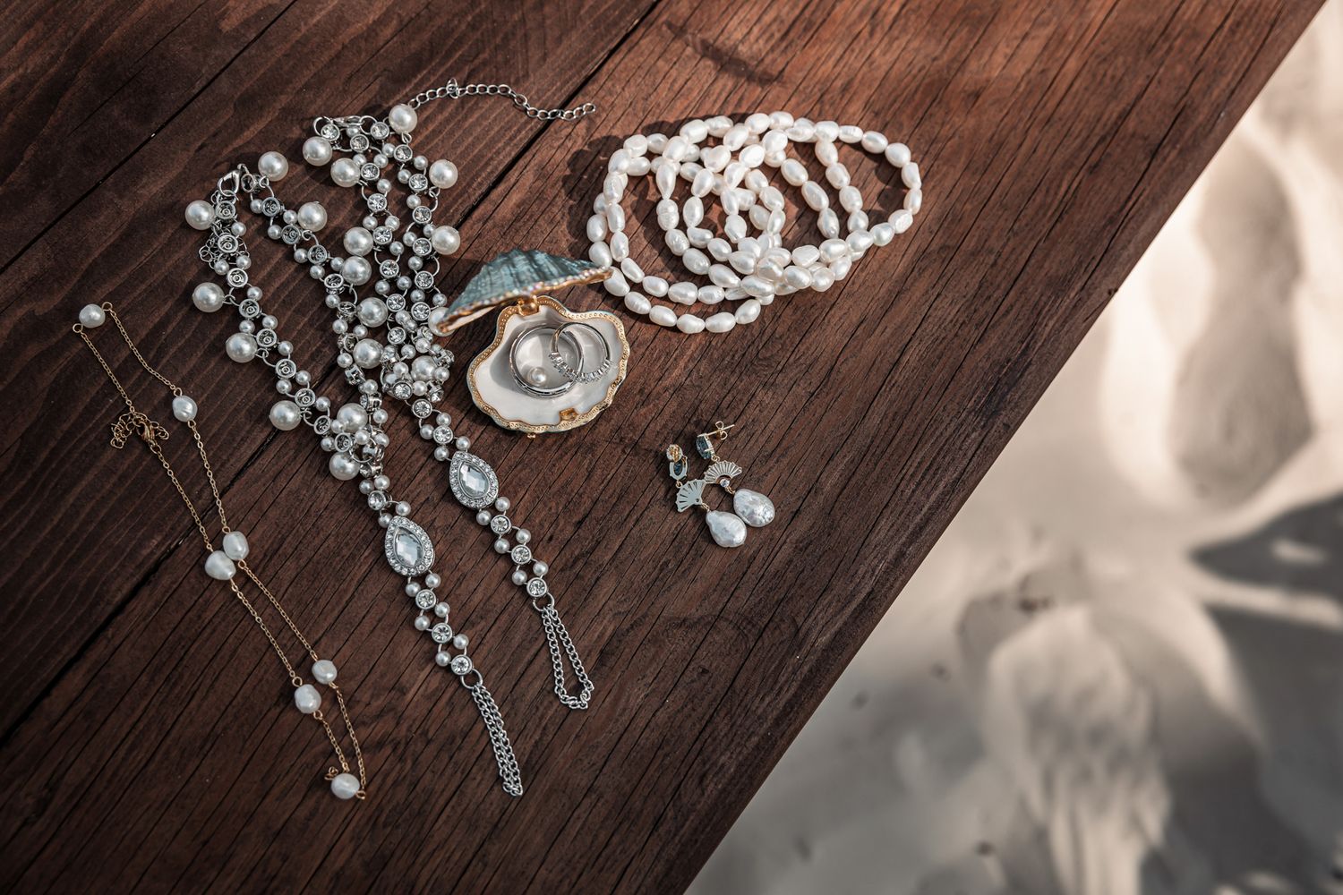 Elegant pearl bracelets, necklaces, and earrings arranged on a rustic wooden surface with a decorative shell centerpiece.