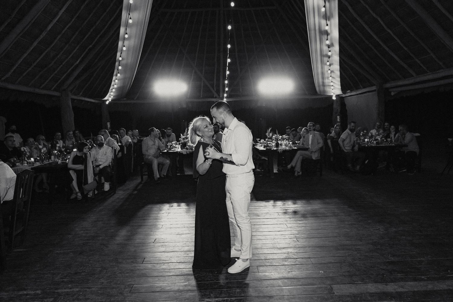Black and white photo of groom sharing emotional dance with mother at wedding reception.