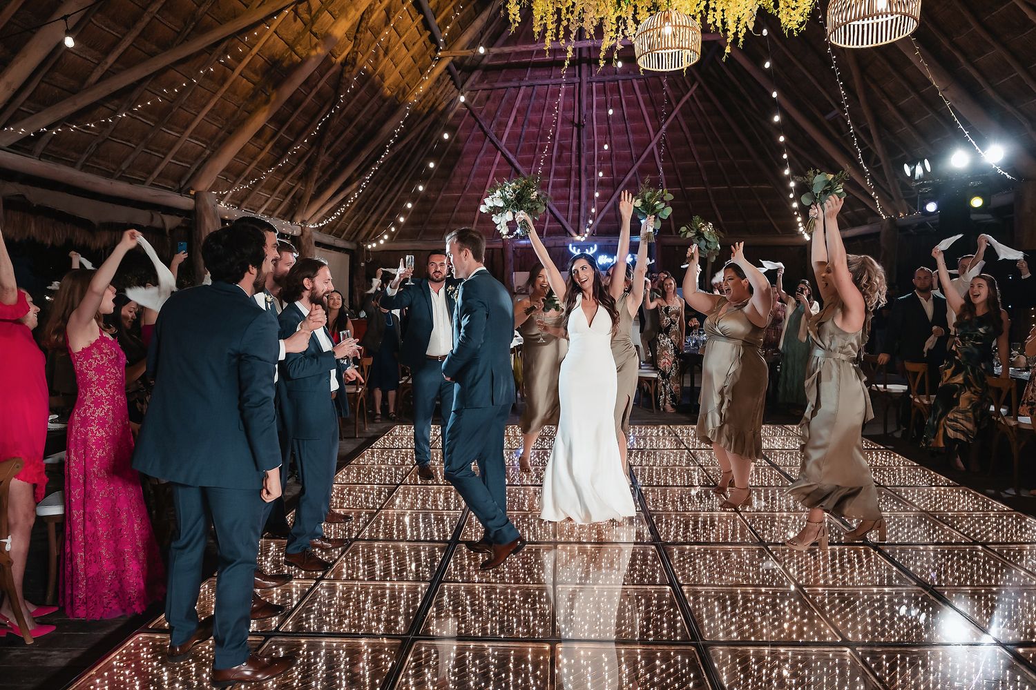 Bride and groom share first dance surrounded by cheering guests on a sparkling dance floor at elegant wedding reception.