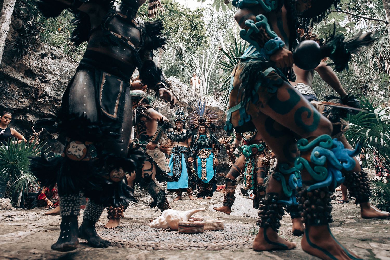 Group of dancers in traditional Mayan ceremonial costumes performing a ritual dance in an outdoor jungle setting.