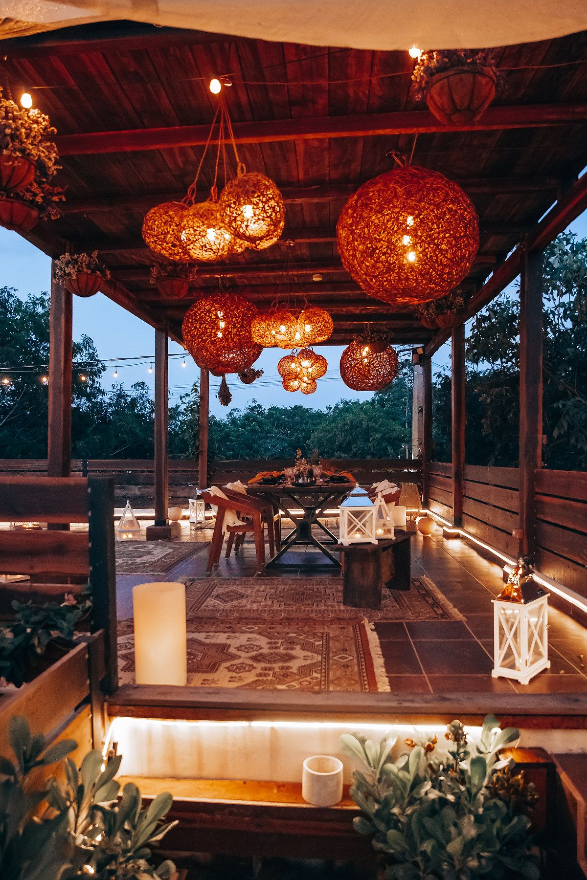 Romantic outdoor wedding reception pavilion with glowing wicker pendant lights and candles at twilight.
