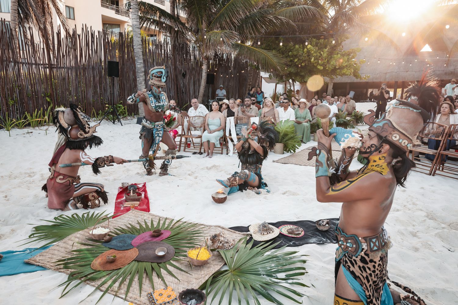 Traditional Mayan performers in ceremonial costumes entertain guests at a beachside cultural event.