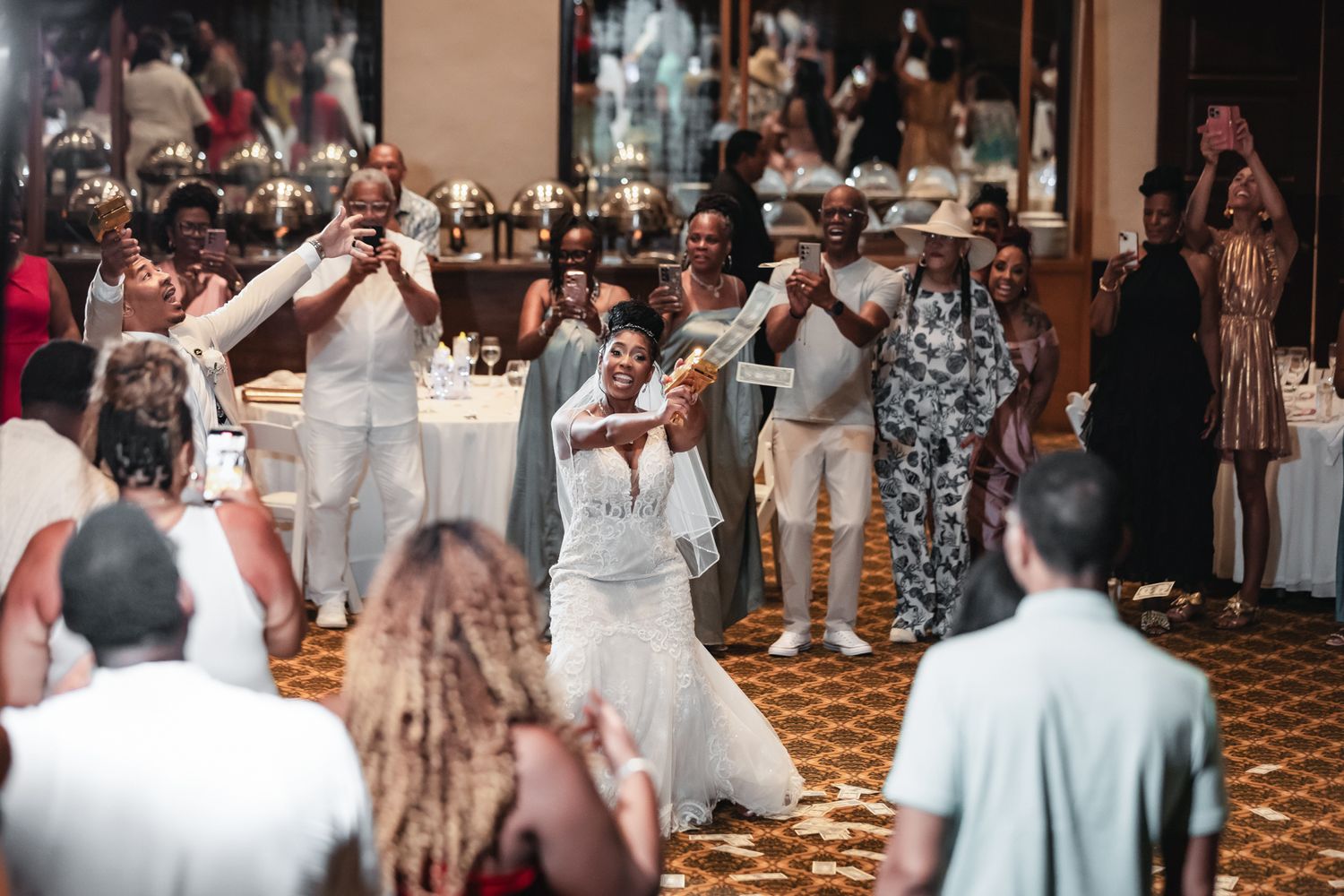 Bride in white gown celebrates with guests at elegant wedding reception in a grand ballroom.