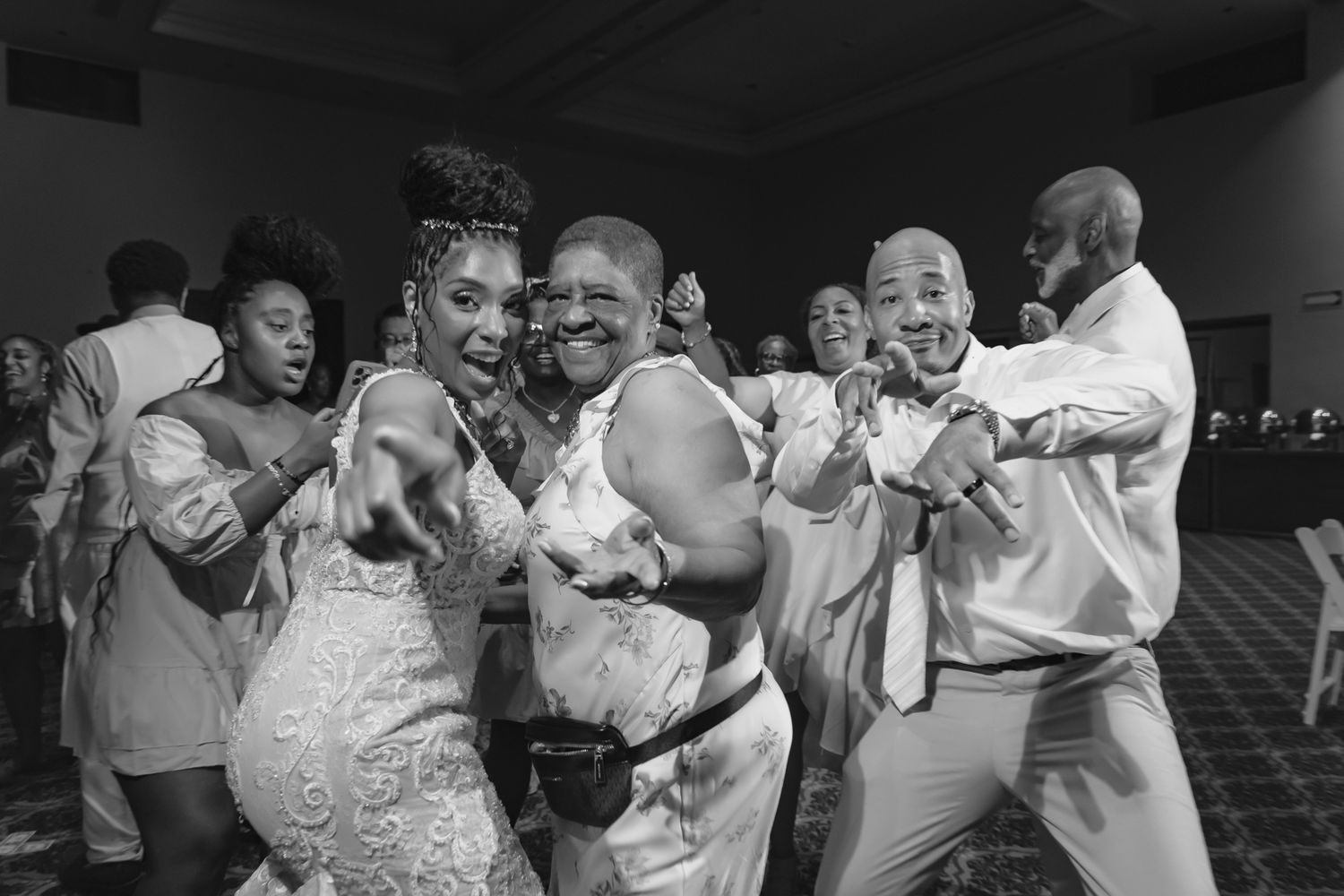 Joyful wedding guests dancing and celebrating at a lively indoor wedding reception in black and white photo.