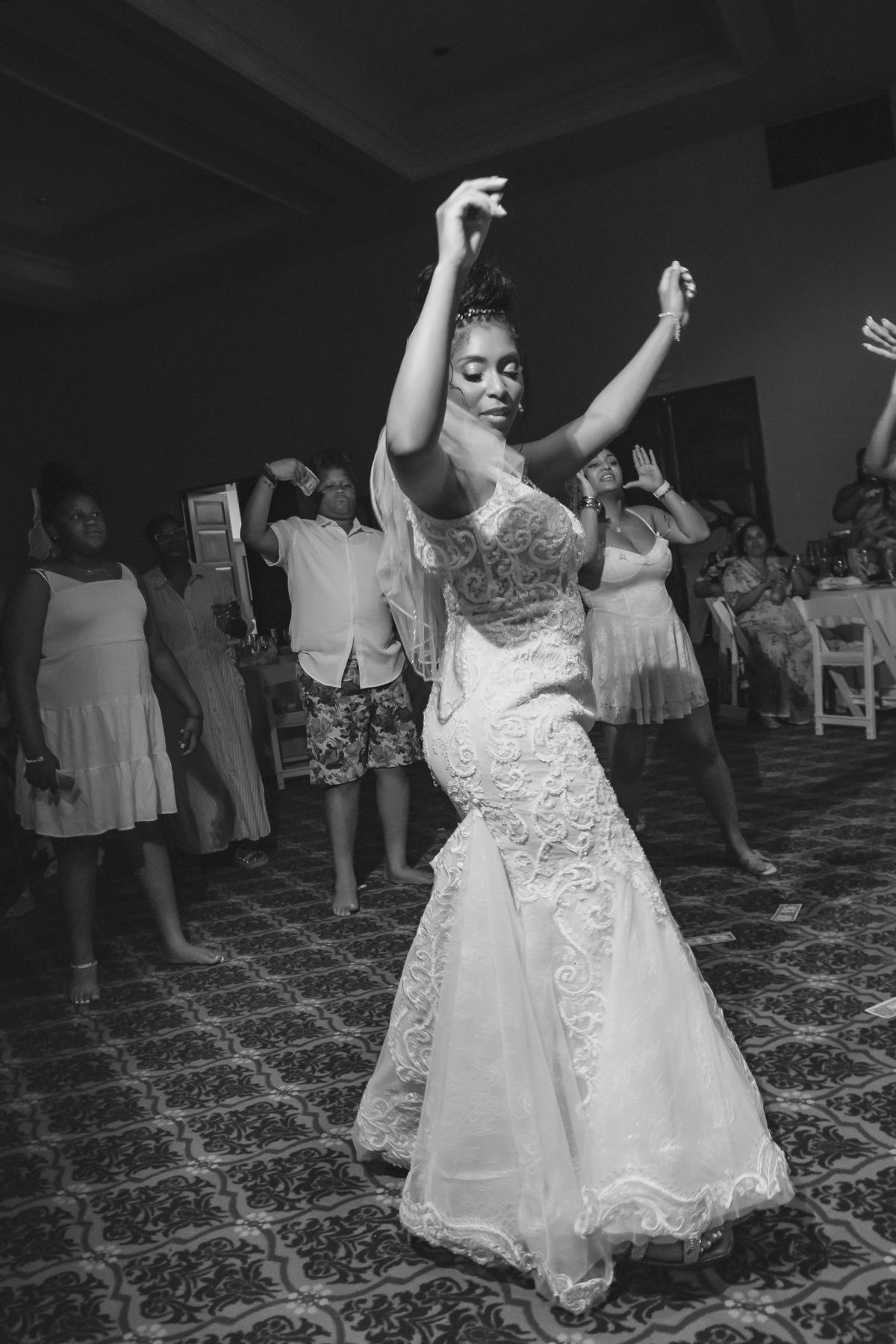 Bride in lace mermaid gown dancing joyfully at wedding reception in black and white photo.