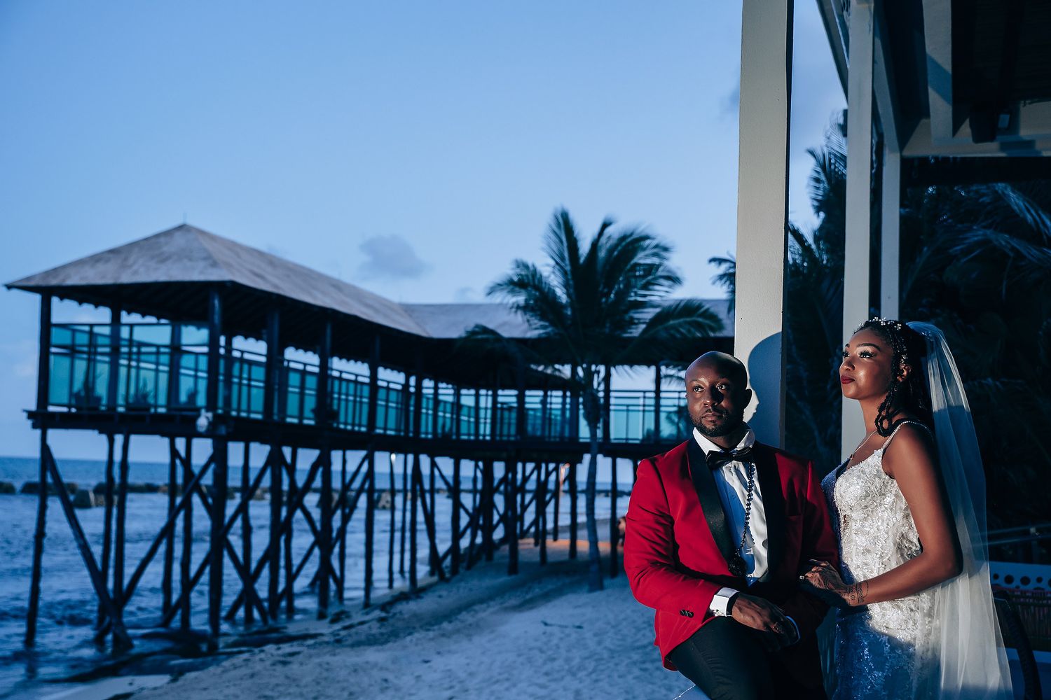 A couple shares a romantic moment at sunset on a wooden pier extending over calm ocean waters.