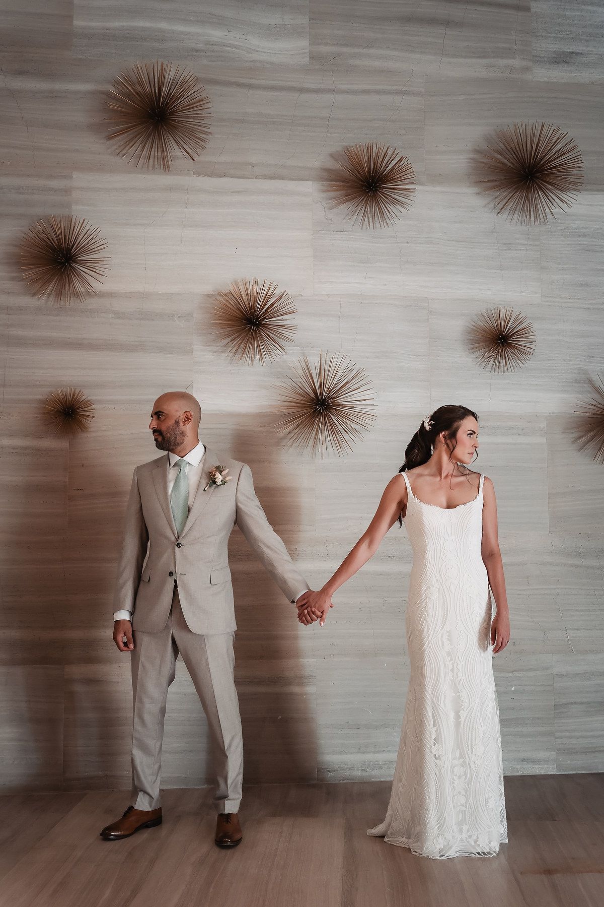 A couple in wedding attire holds hands against a wall decorated with starburst wall art decorations.