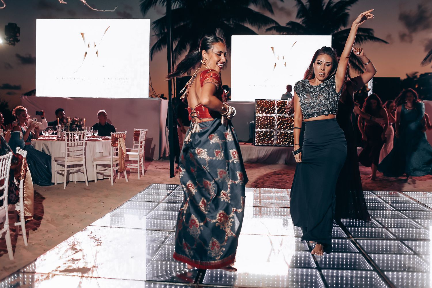 People dancing at a wedding reception on a checkered dance floor with white chairs in the background.