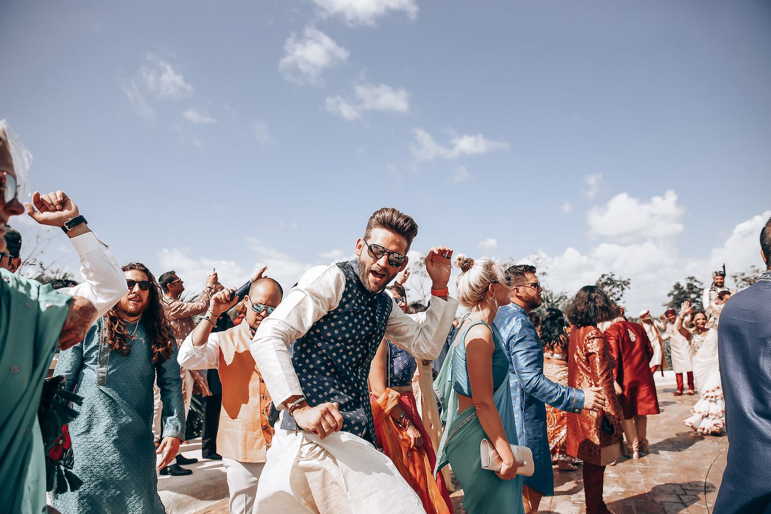 A joyous celebration with people dancing outdoors under a bright blue sky.