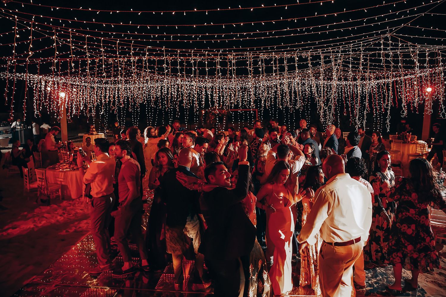 A crowded dance floor illuminated by red lighting shows people dancing and socializing at a nightclub event.
