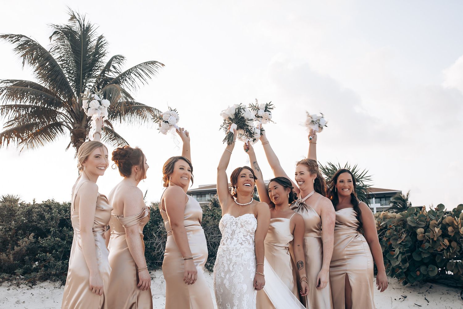 Wedding party celebrates on beach in coordinated light colored attire.