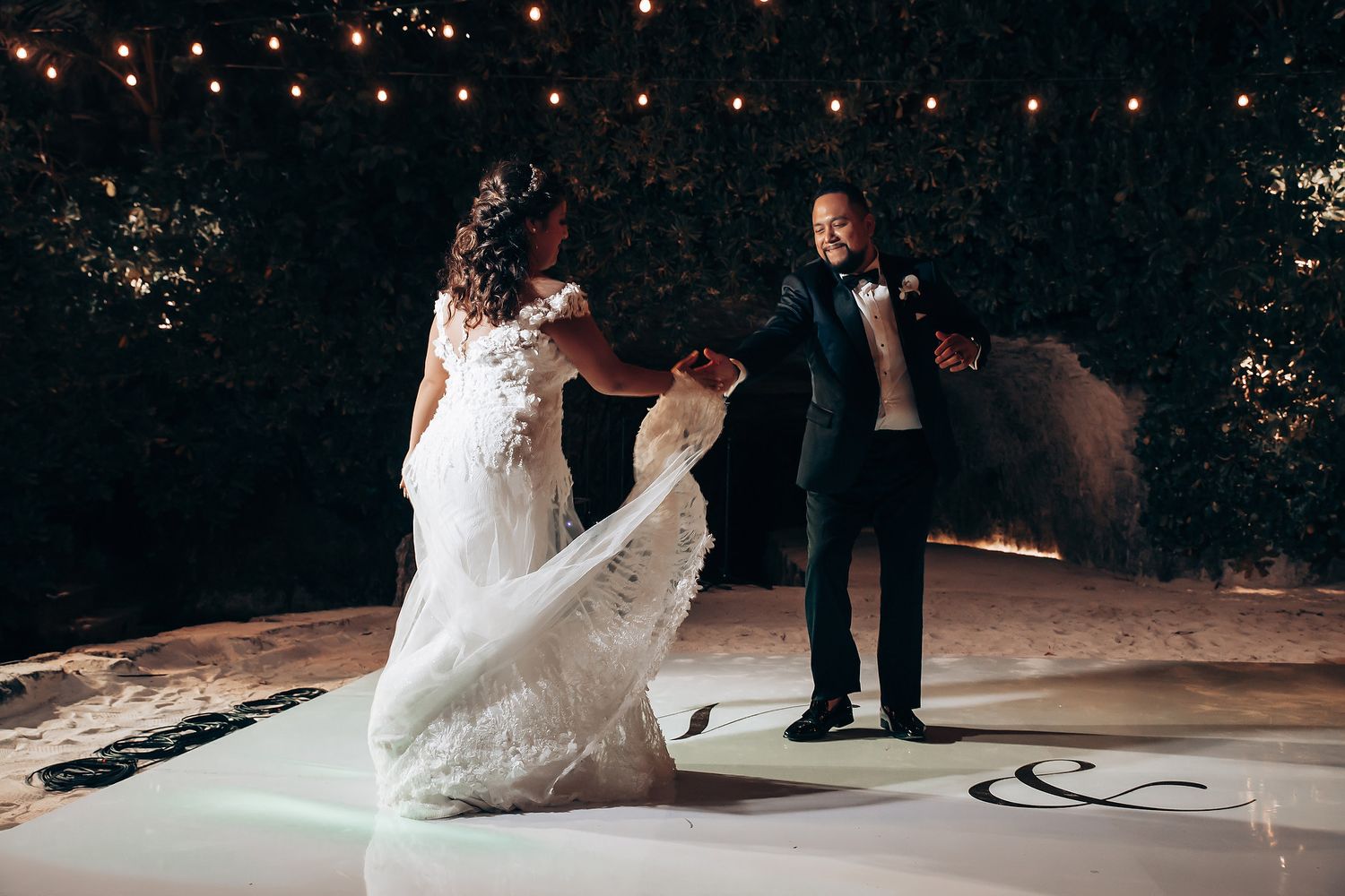 Couple shares their first dance under twinkling lights on an elegant white dance floor.