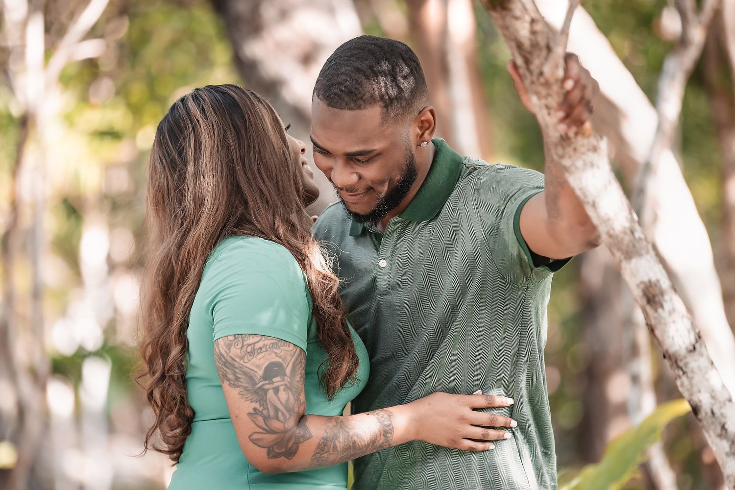 A couple wearing matching green outfits embrace in a romantic outdoor photoshoot among trees.