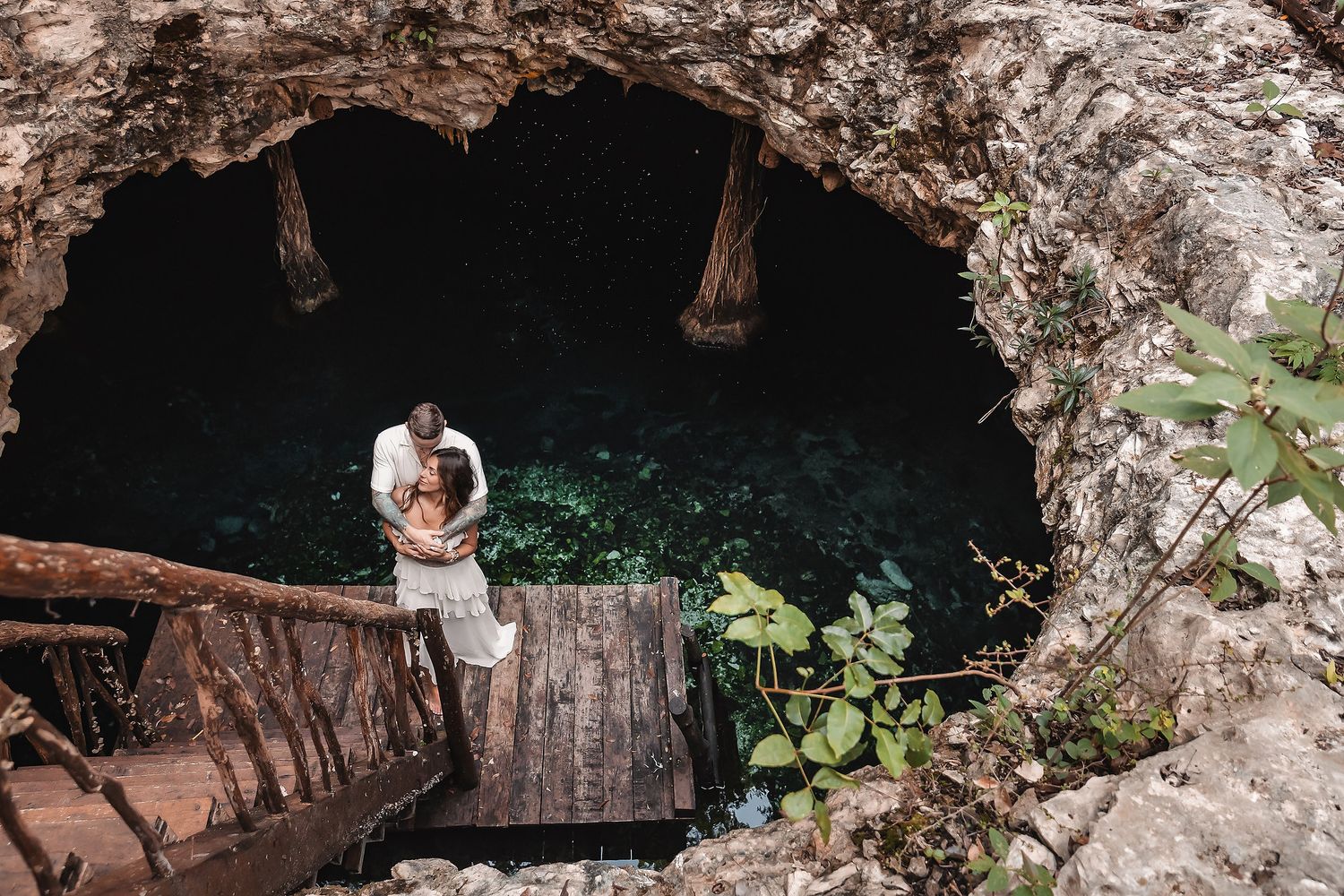 A couple explores a scenic cave entrance with wooden stairs and natural rock formations.