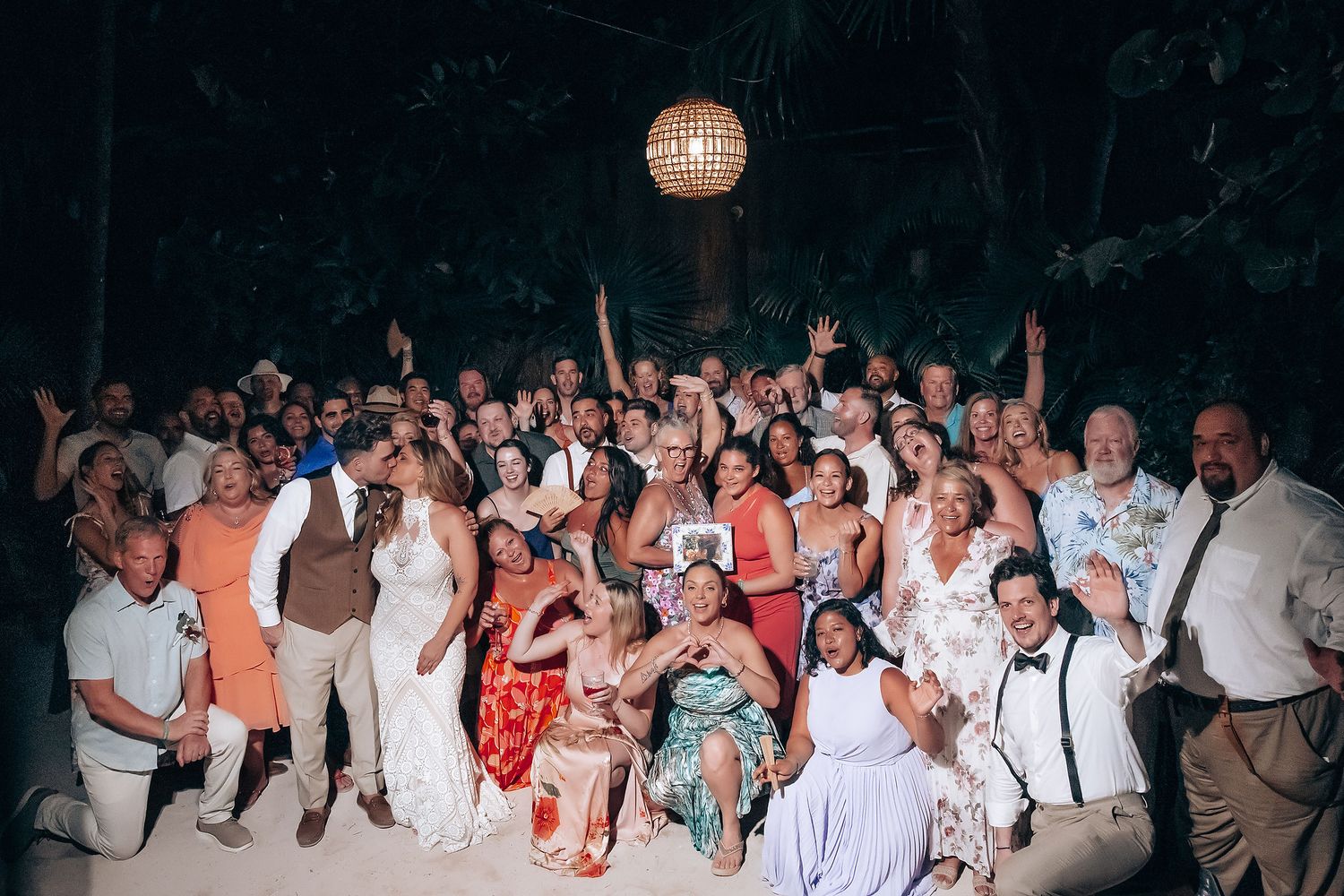 Wedding guests dance and celebrate together on a dimly lit dance floor during an evening reception.