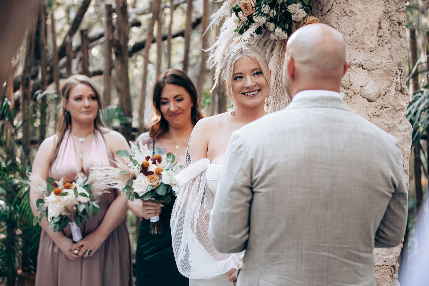 Wedding party gathers outdoors for candid moments with bouquets of peach and white flowers during a garden celebration.