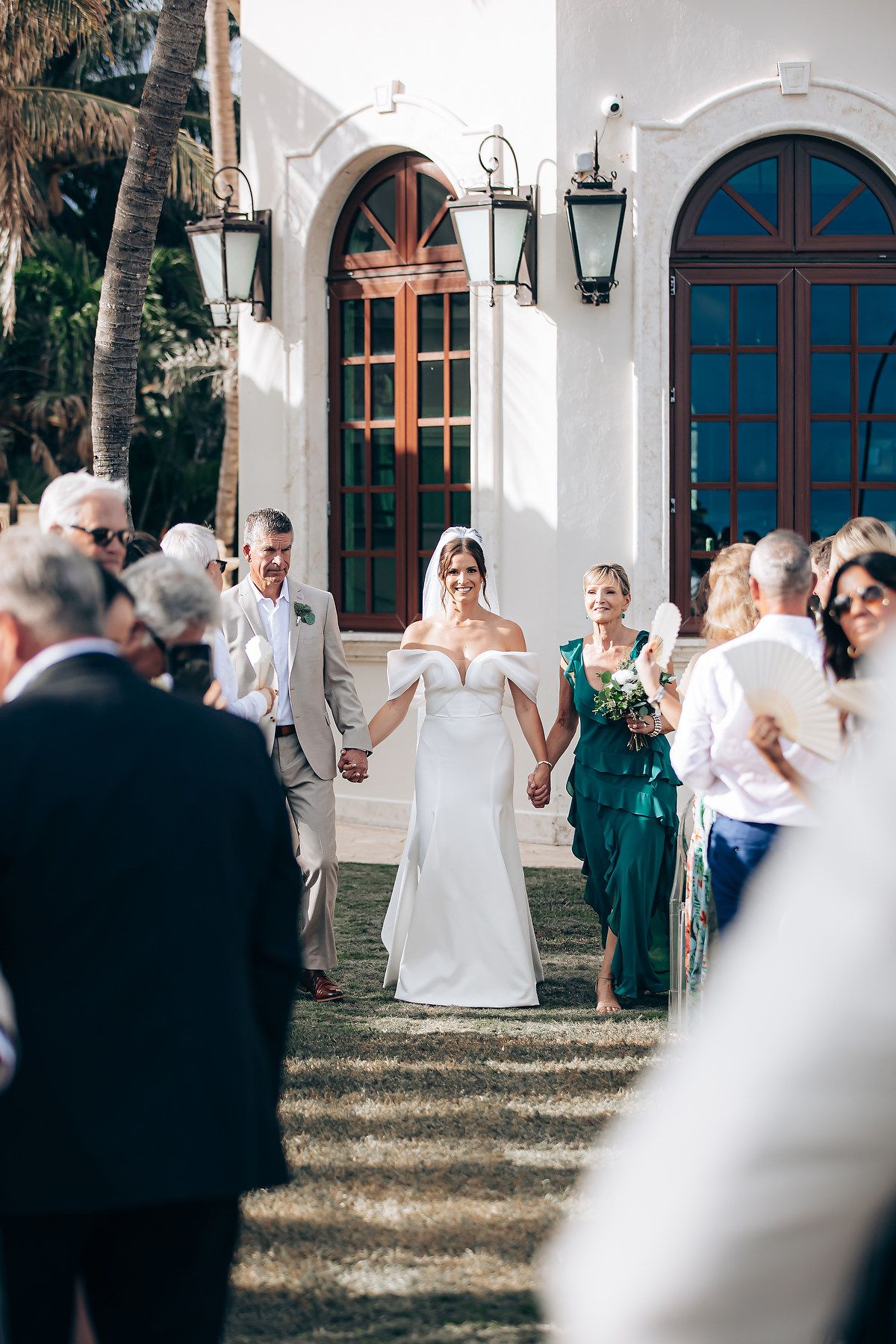 Wedding ceremony takes place outside a white Spanish colonial style church with arched doorways and lanterns.