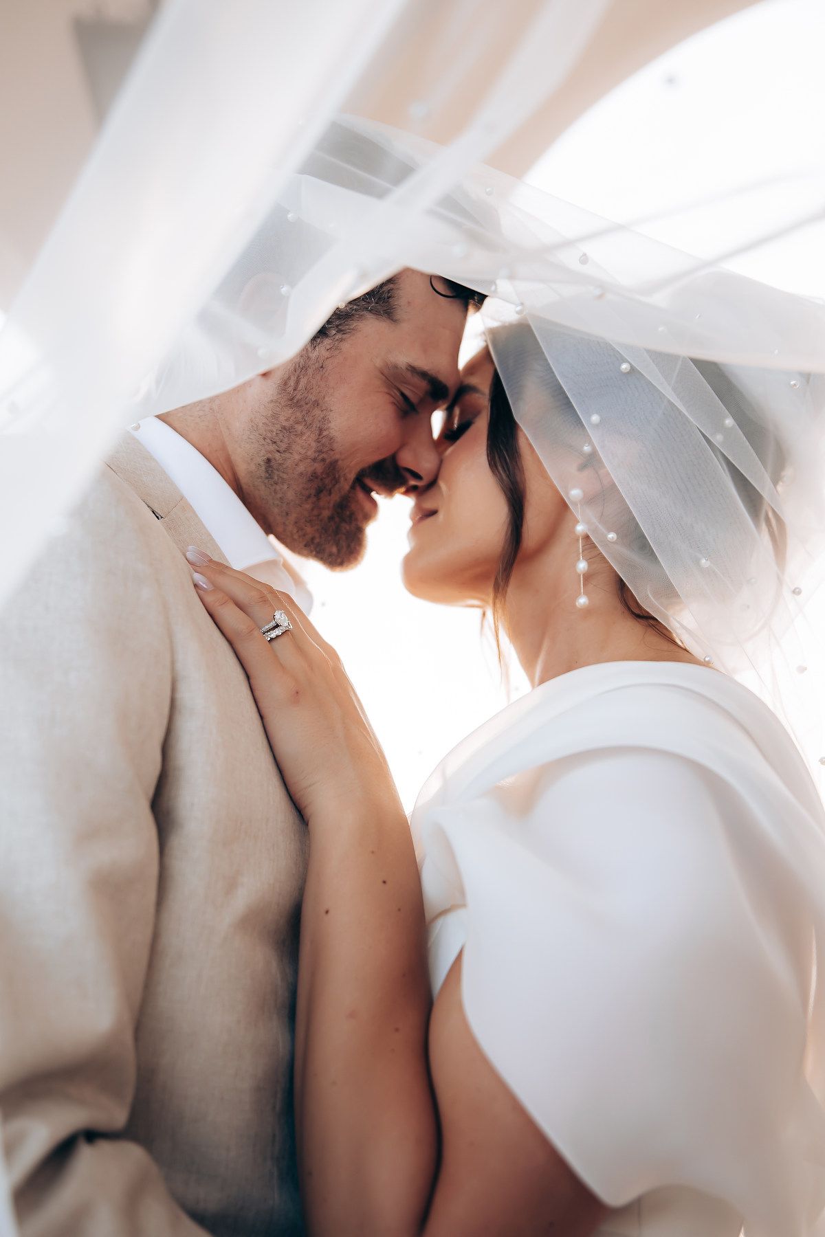 A romantic wedding moment captured as a couple shares an intimate kiss under a flowing white veil.