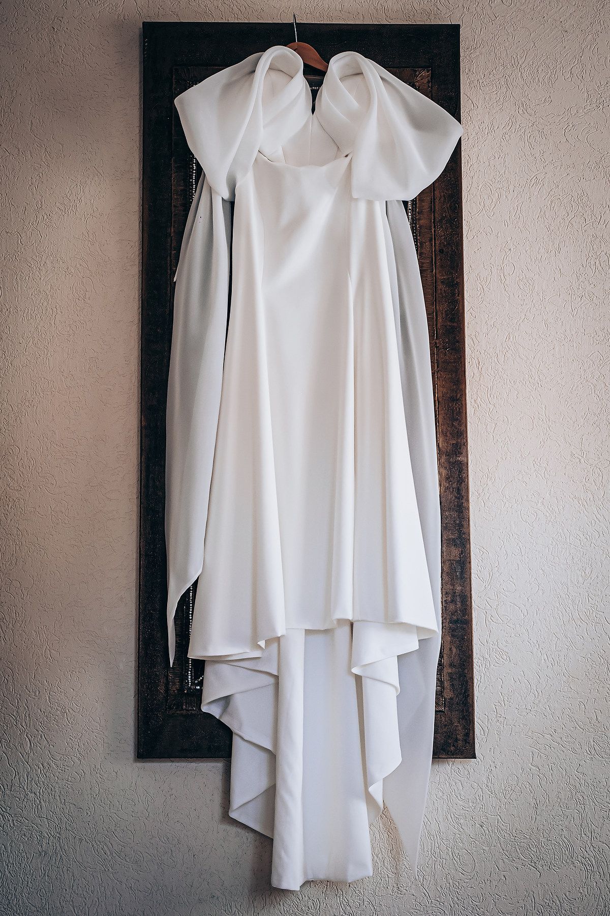 A white flowing dress shirt with cascading layers hangs against a textured wall in multiple angles.
