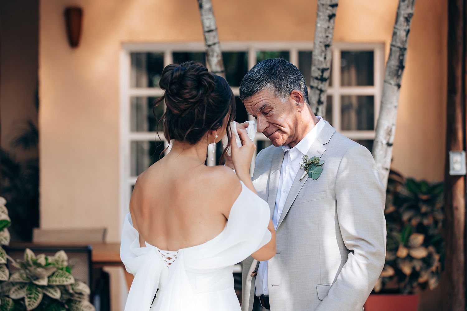 A couple shares a tender moment during their wedding ceremony, with the bride in white and groom in light attire.