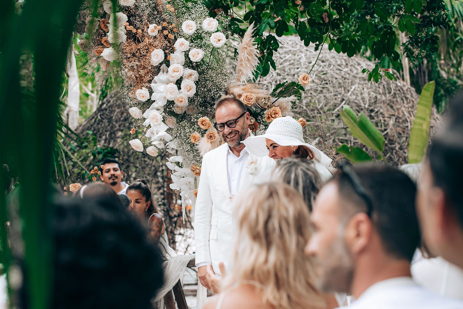 Wedding guests gather outdoors under a rustic stone archway during a sunny celebration.