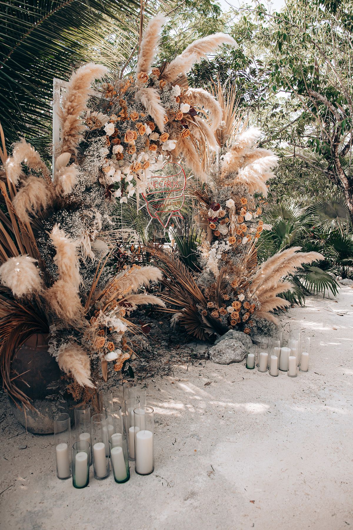 Dried pampas grass arrangements with frosted glass vases create a bohemian wedding ceremony backdrop in natural light.