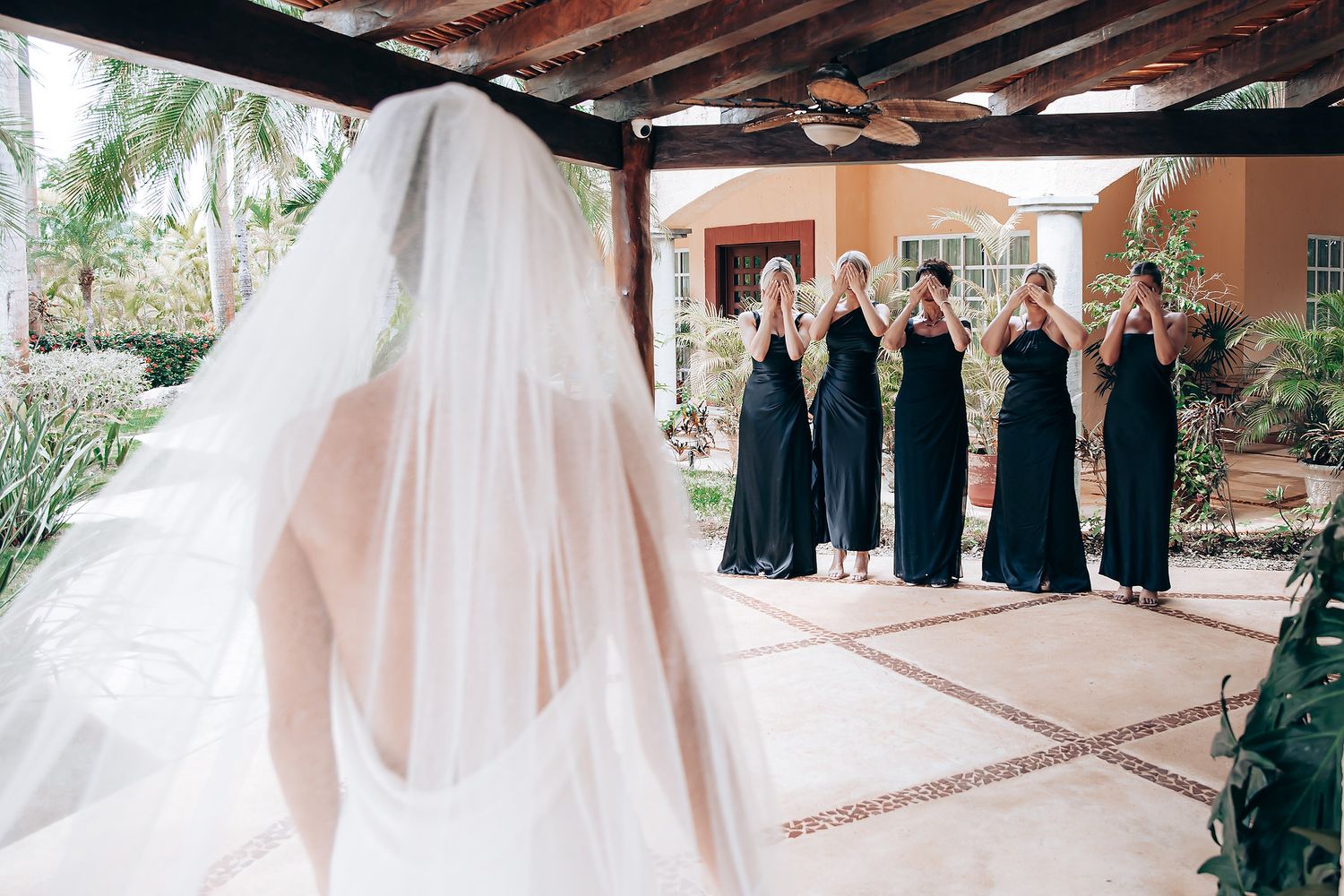 Bridesmaids in navy blue dresses react emotionally as they see the bride in her flowing white veil.