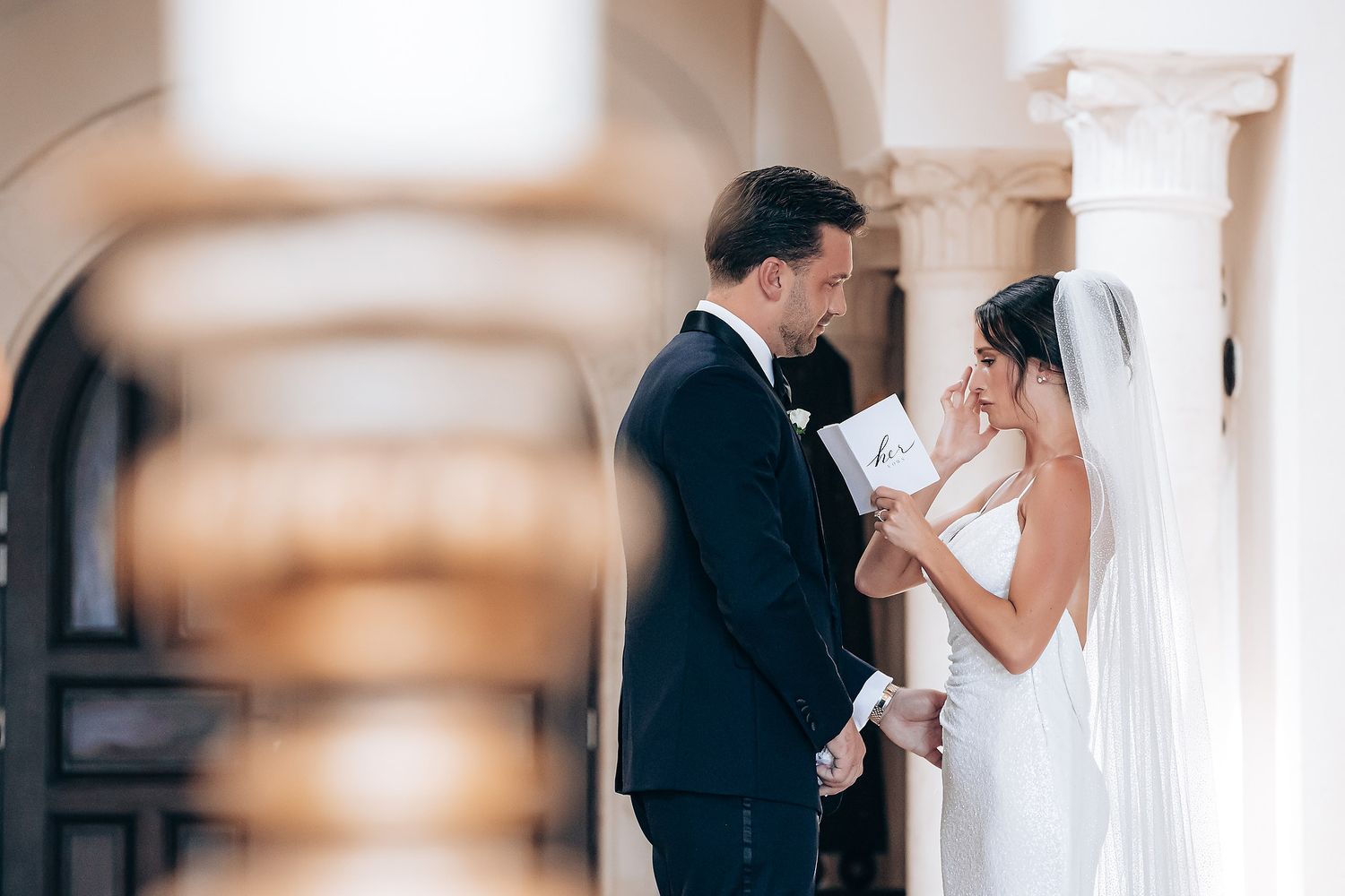 A couple in formal wedding attire shares an intimate kiss during their wedding ceremony in an elegant venue.