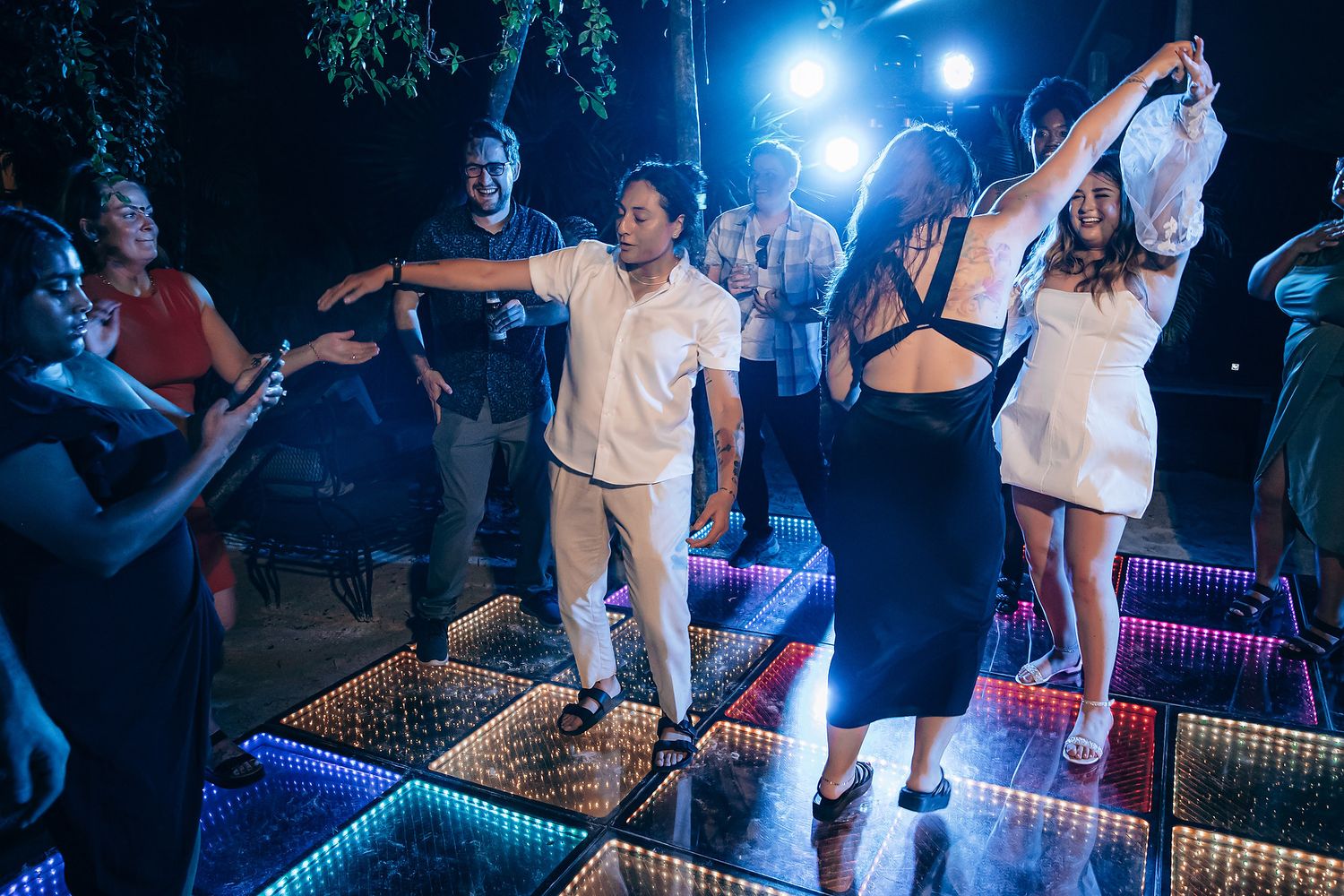 People enjoying themselves on a colorfully lit dance floor at a nighttime event.