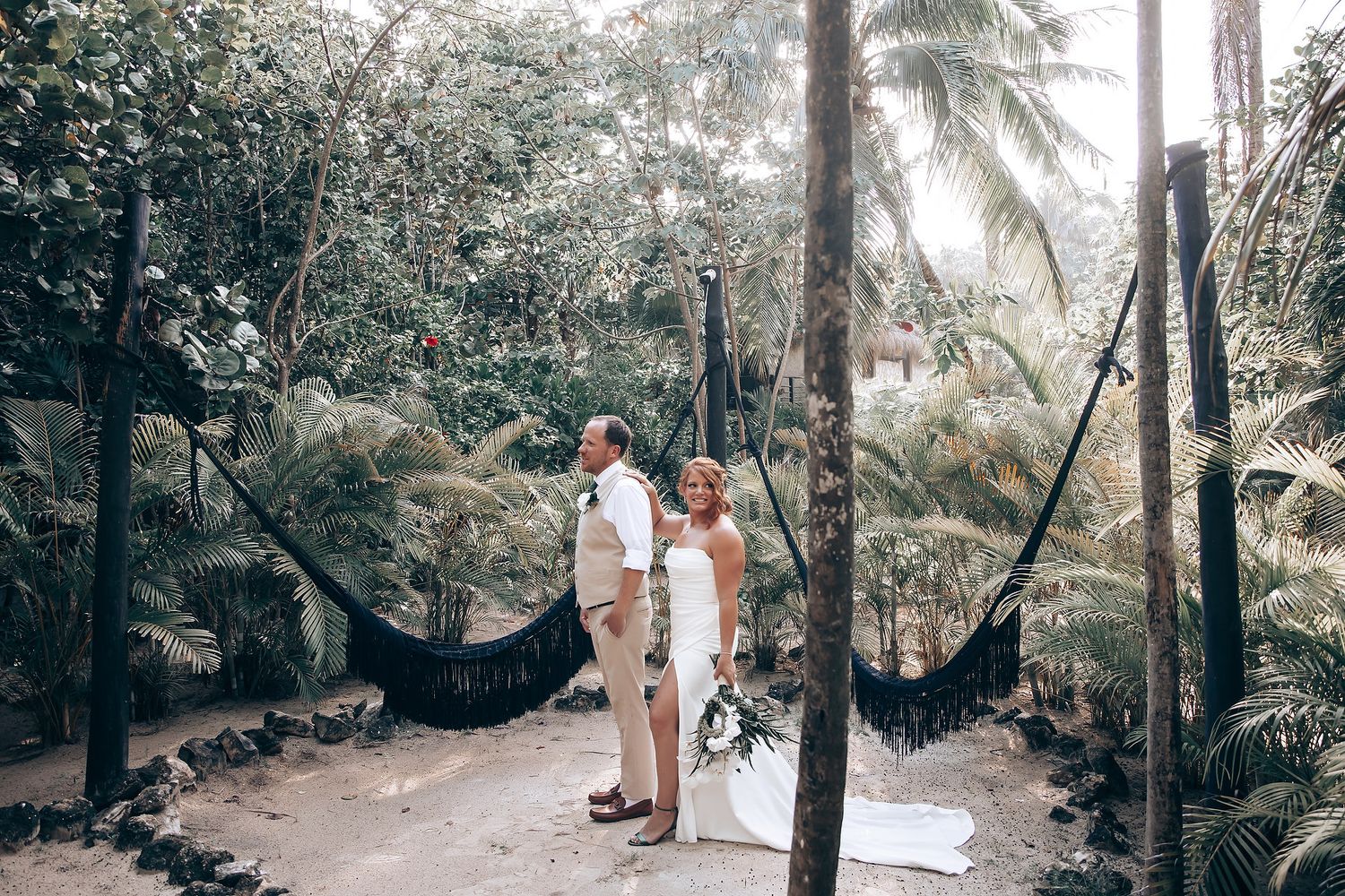 Wedding couple poses playfully on a path surrounded by lush tropical foliage.