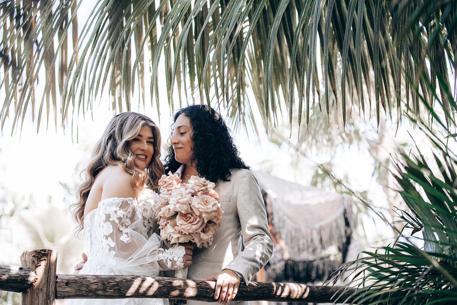 Two people share a tender moment under palm fronds in a tropical setting.