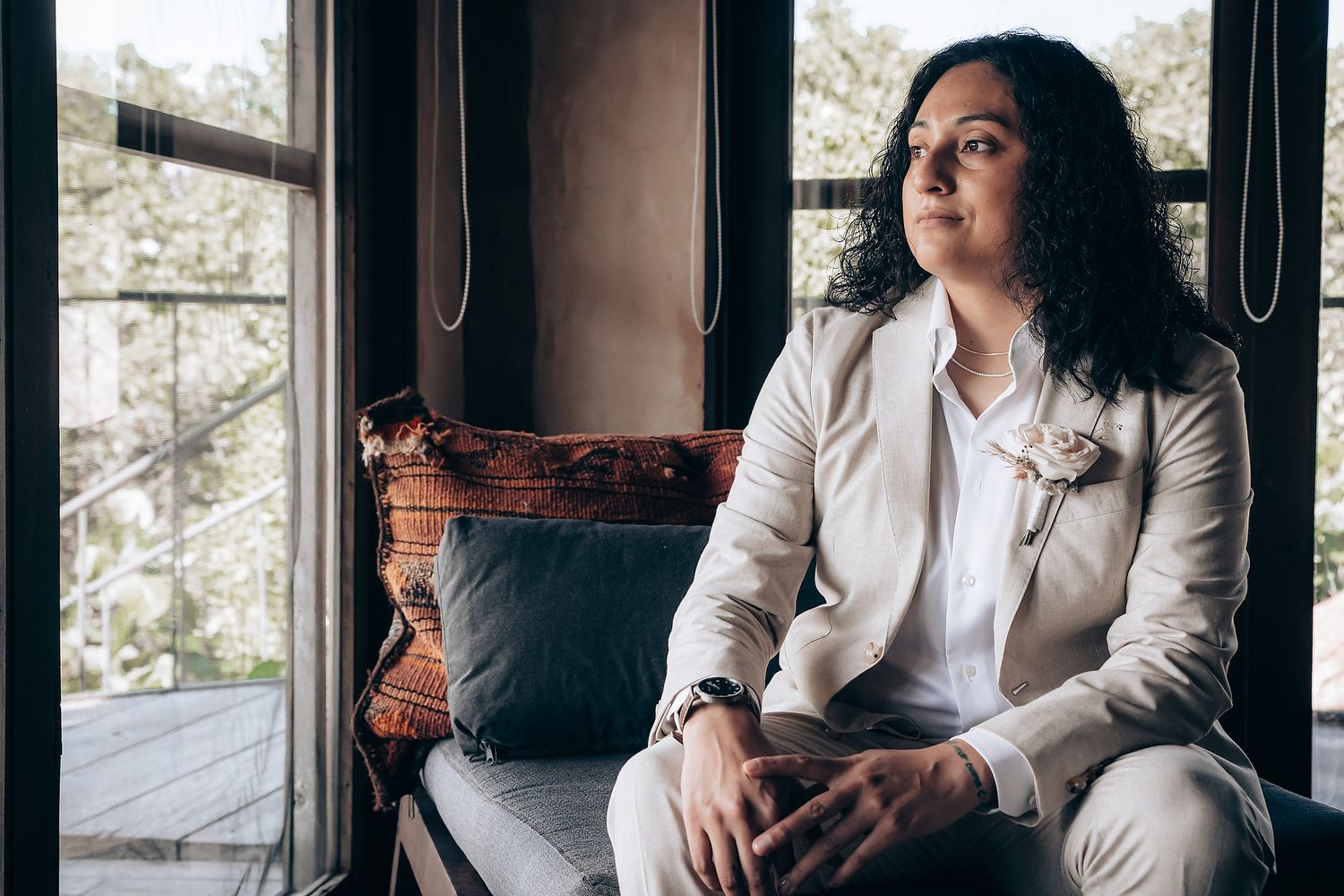 Professional woman in white blazer sits thoughtfully by window in modern office setting.