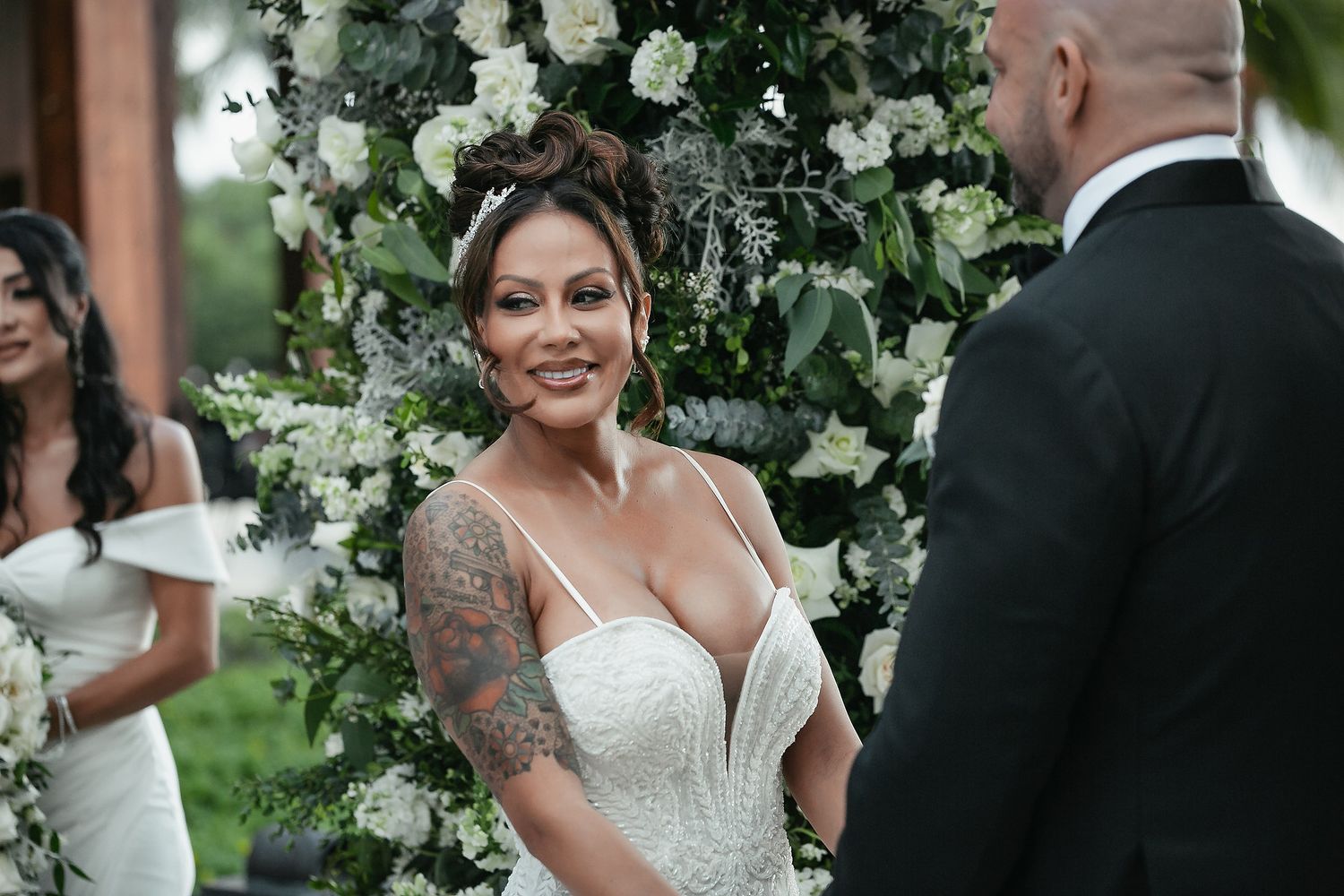 A happy couple shares a joyful moment surrounded by elegant white floral arrangements at an outdoor wedding ceremony.