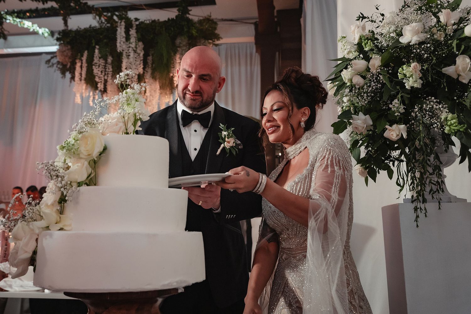 A wedding reception scene with floral arrangements and white decor in an elegant indoor venue.