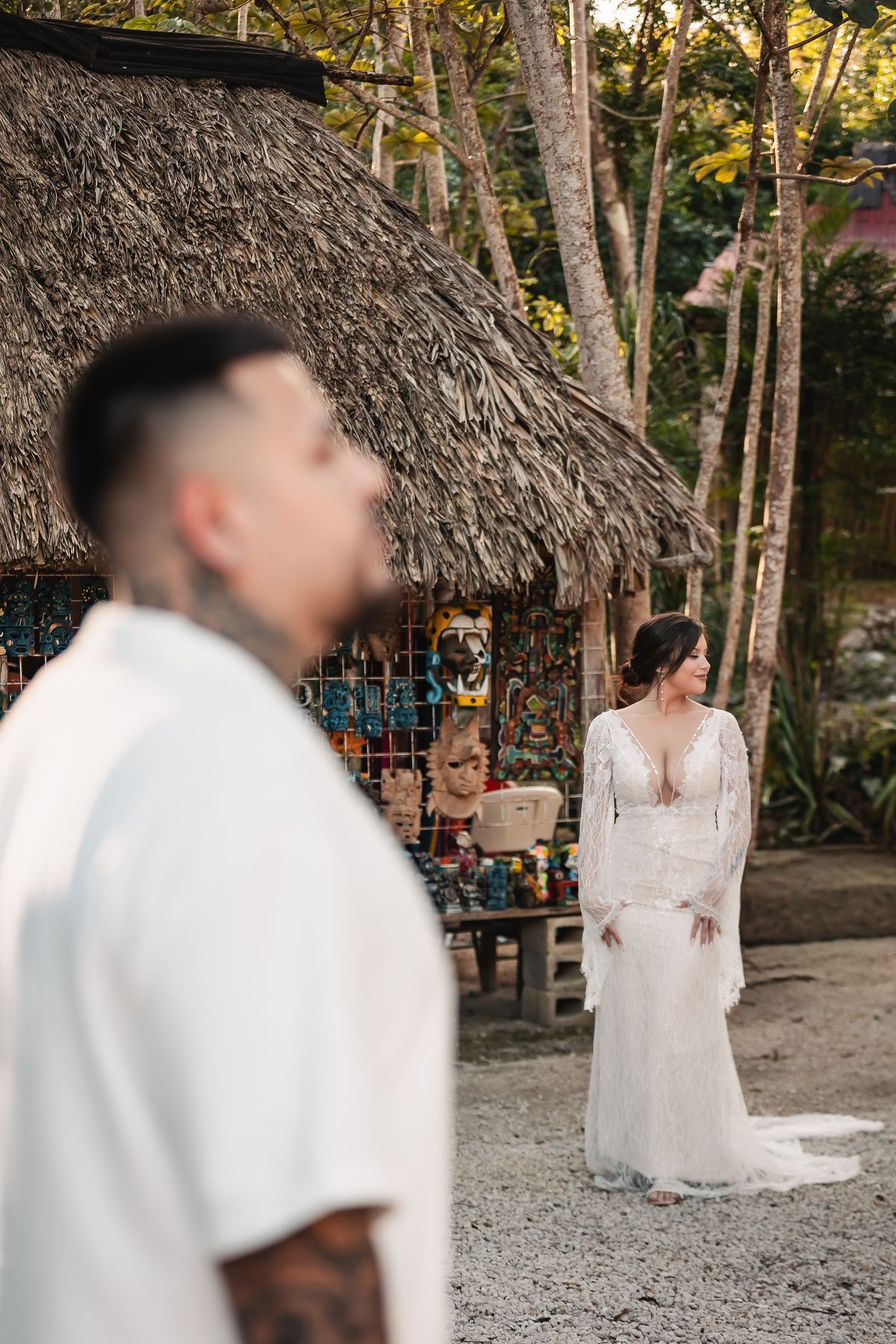 A romantic wedding photo captured under a thatched roof structure with rustic decor.