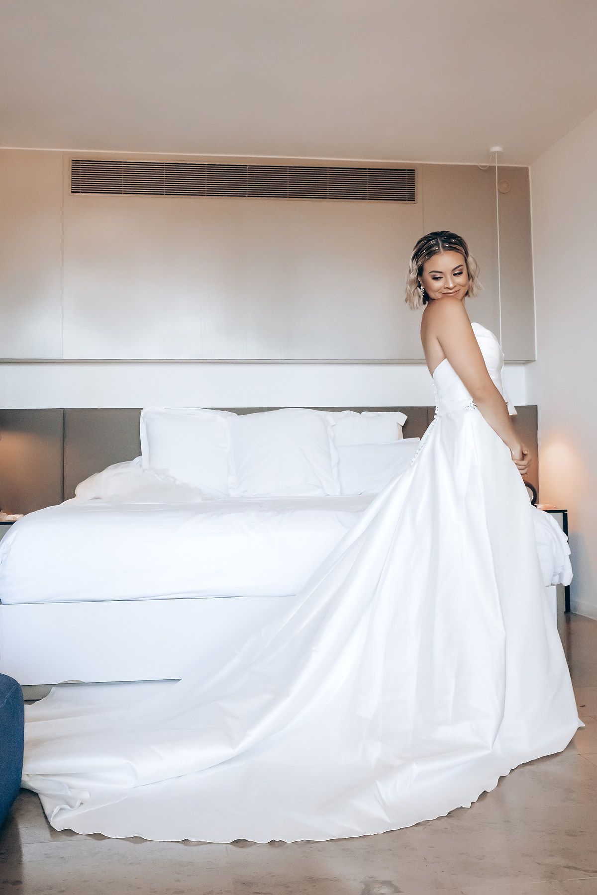 Long flowing white wedding dress train spread across light colored floor.