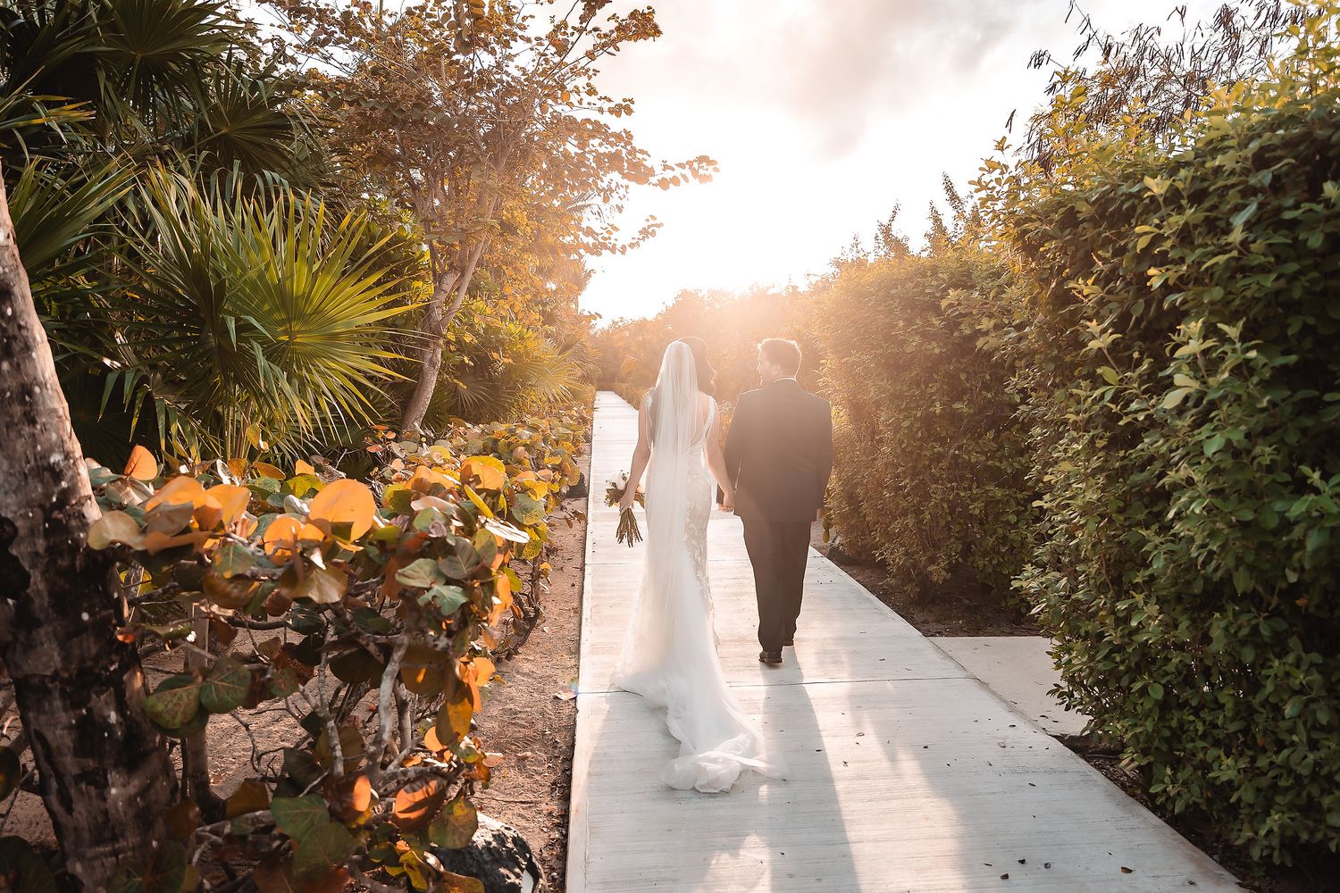 Wedding couple walks along a scenic garden path during golden hour.