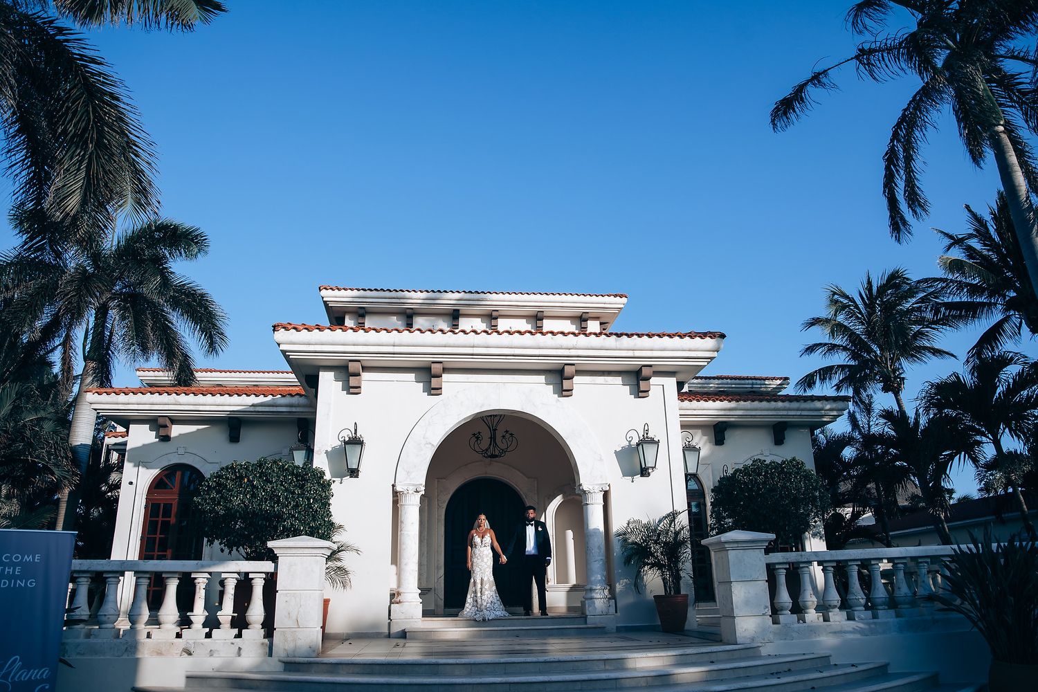 Mediterranean-style white stucco wedding venue with palm trees against blue sky.